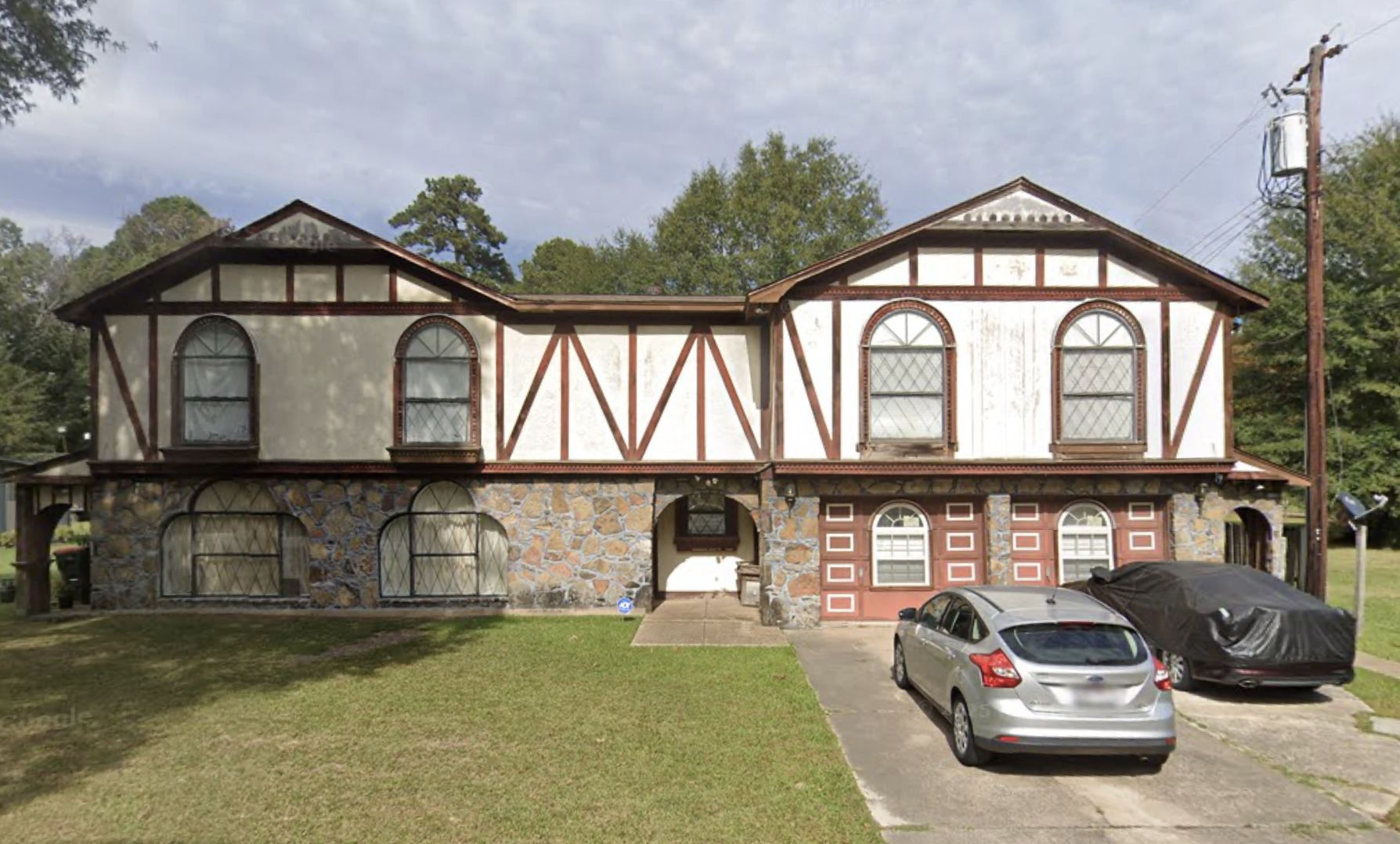 A two story house with a grassy lawn and two vehicles parked in the driveway.